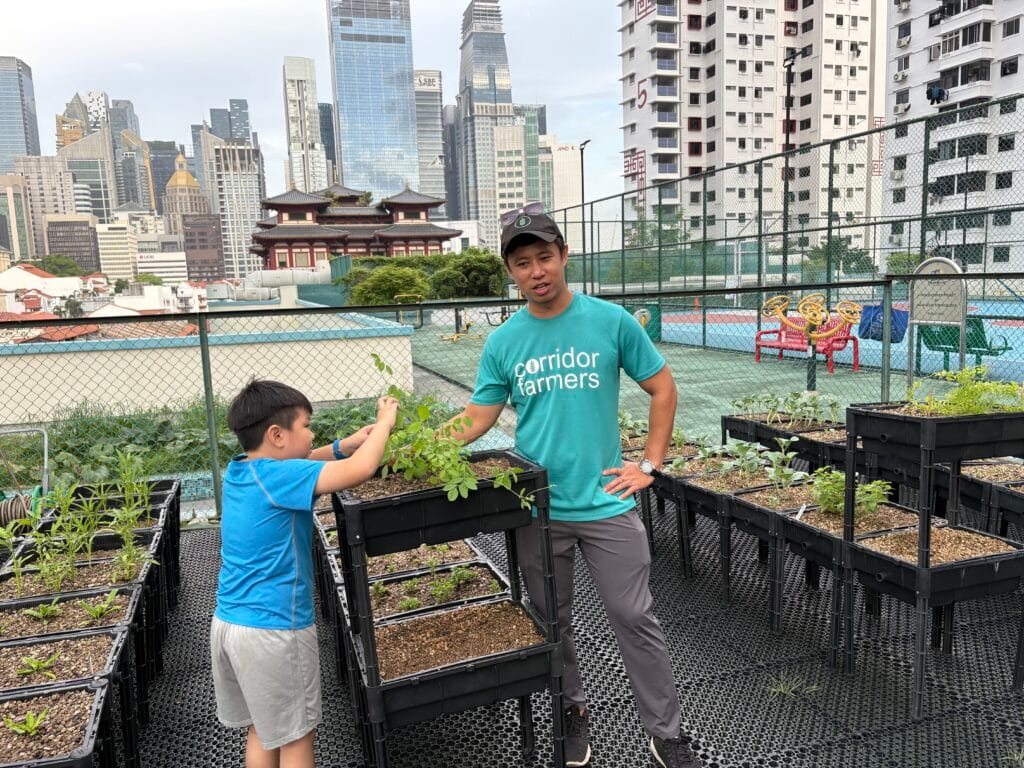 Rooftop farmer showing raised plots to a child, with Singapore skyline as backdrop