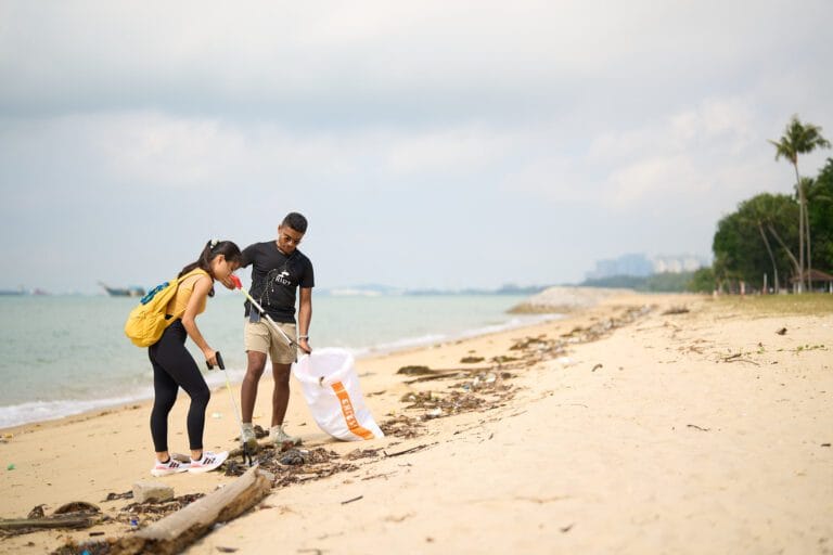 Two people picking up litter with trash pickers on the beach, Yasser on the right